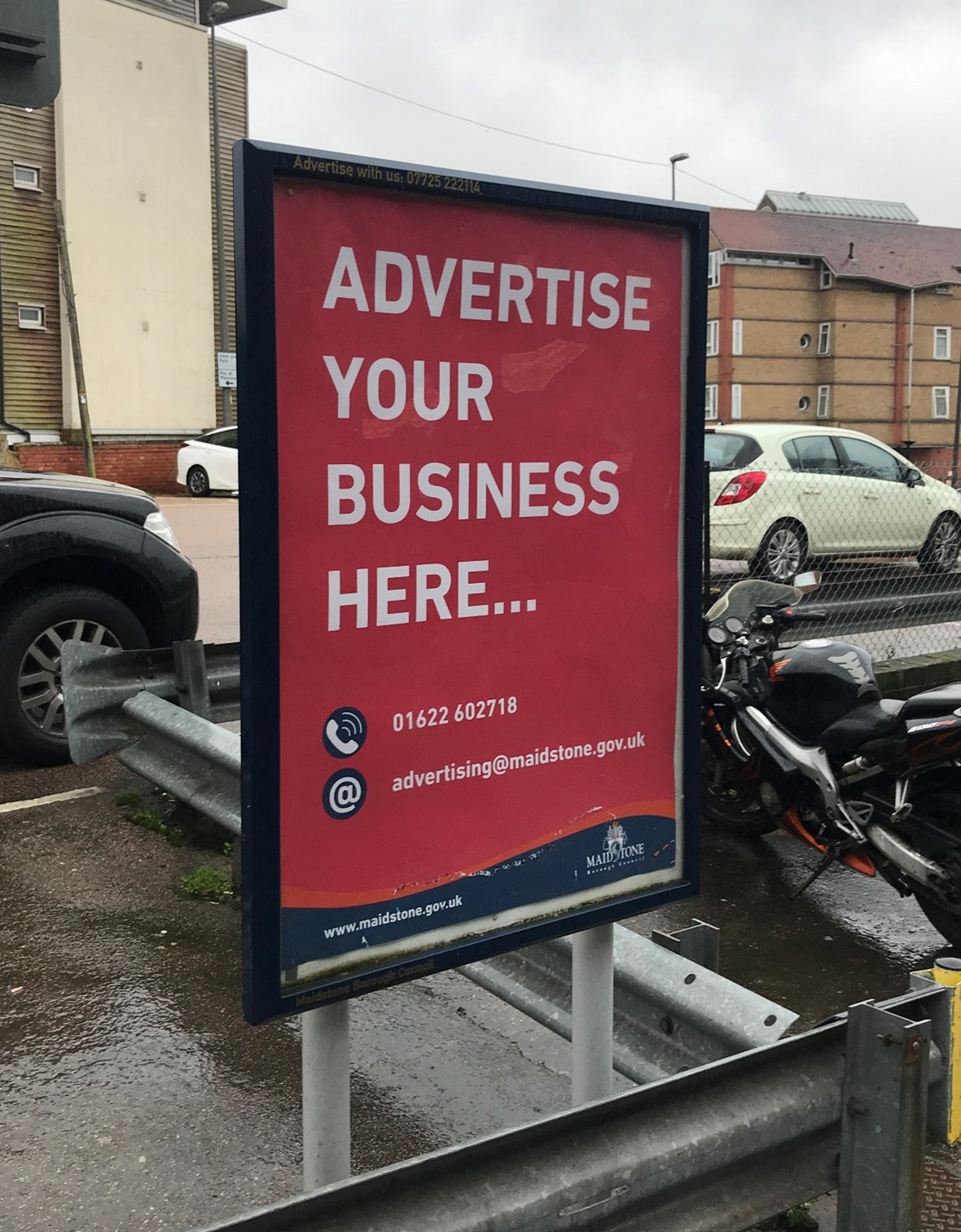 An example of an advertising board. It shows a black frame in a public space with a poster that reads 'advertise your business here