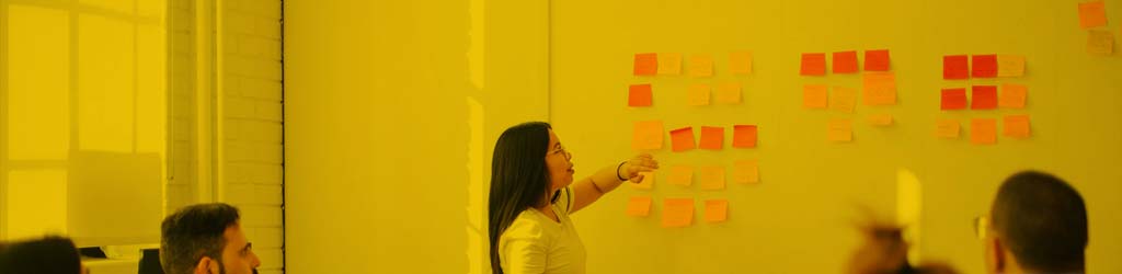 A woman pointing at sticky notes on a wall during a meeting.