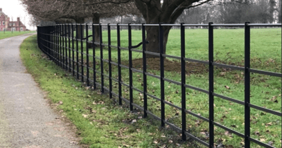 A low-level fence formed of metal bars. The vertical uprights are spaced approximately 1m apart, with 5No. round bars, approximately 300mm in diameter, forming the rails of fence.