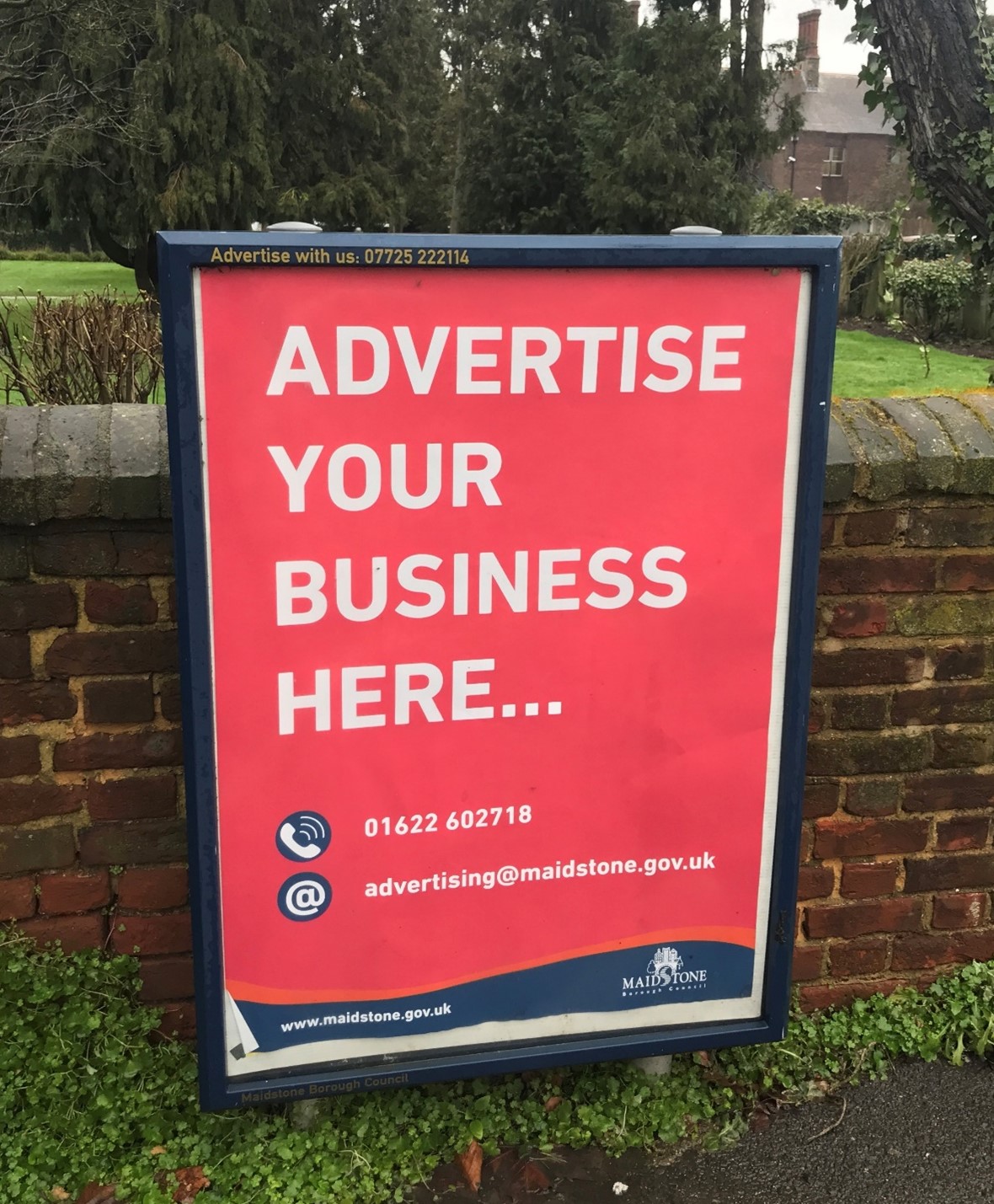 An example of an advertising board. It shows a black frame in a public space with a poster that reads 'advertise your business here